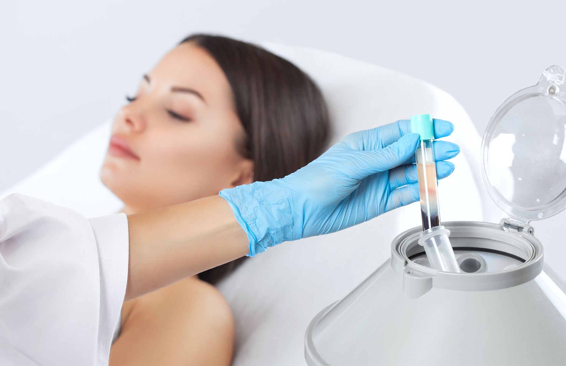 Woman receiving blood sample, doctor in blue gloves placing a vial into a centrifuge.