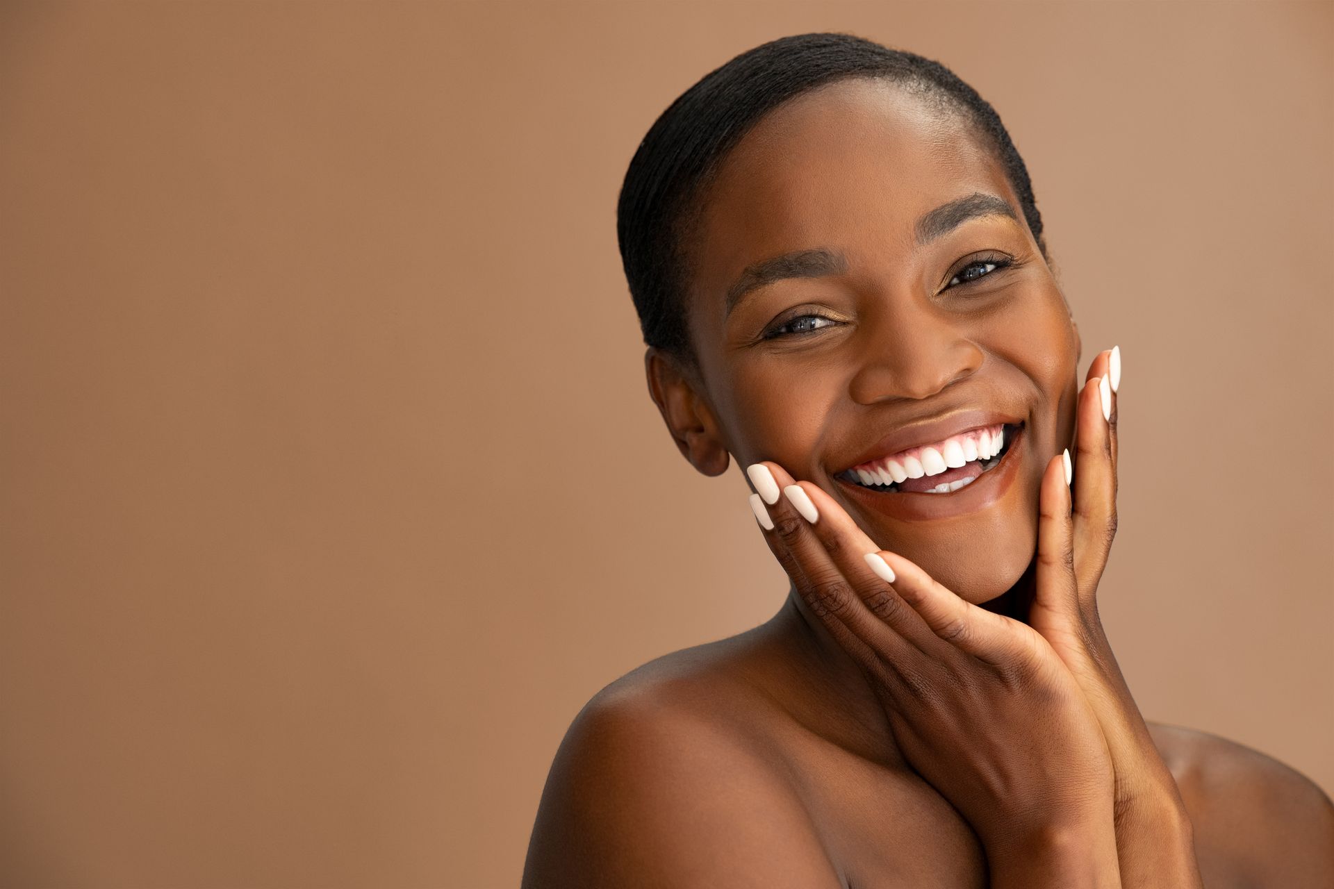 Smiling person with hands on cheeks against a warm tan background