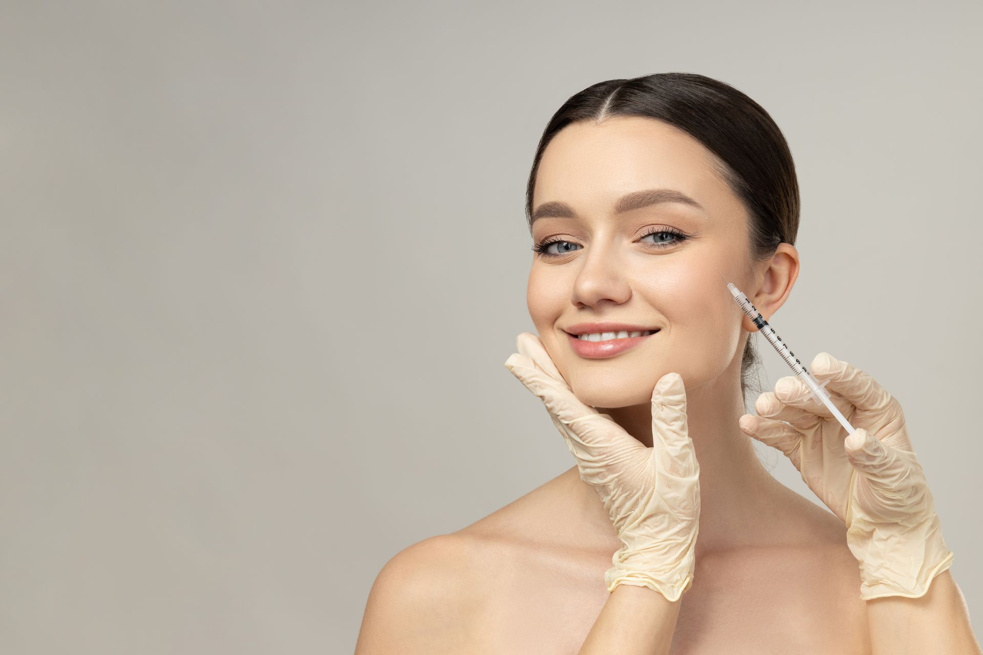 Woman receiving facial injection, smiling, holding face, wearing gloves.
