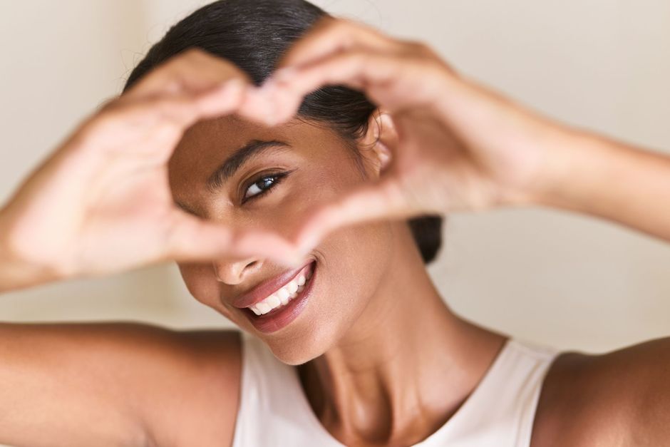 Woman smiles, making a heart shape with her hands.