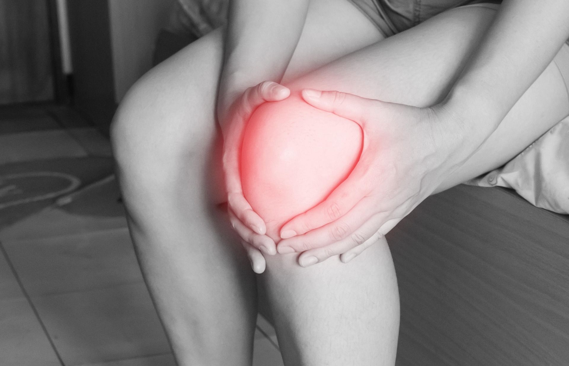 Person holding a glowing red heart shape over their knee in a grayscale room