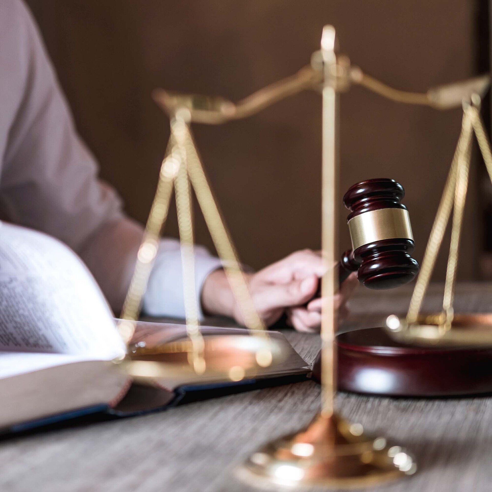 A person is holding a gavel in front of a scale of justice.