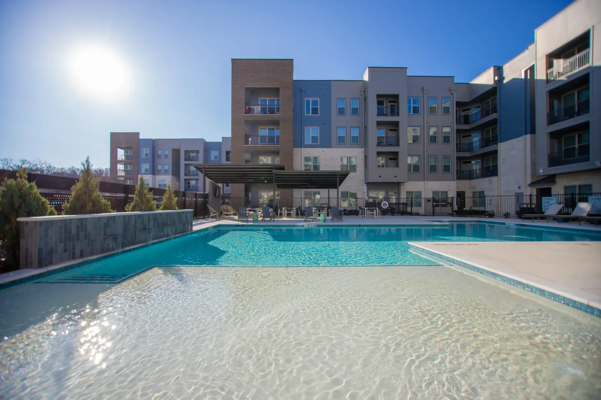 Outdoor apartment community pool with lounge chairs and modern mid-rise buildings in the background.