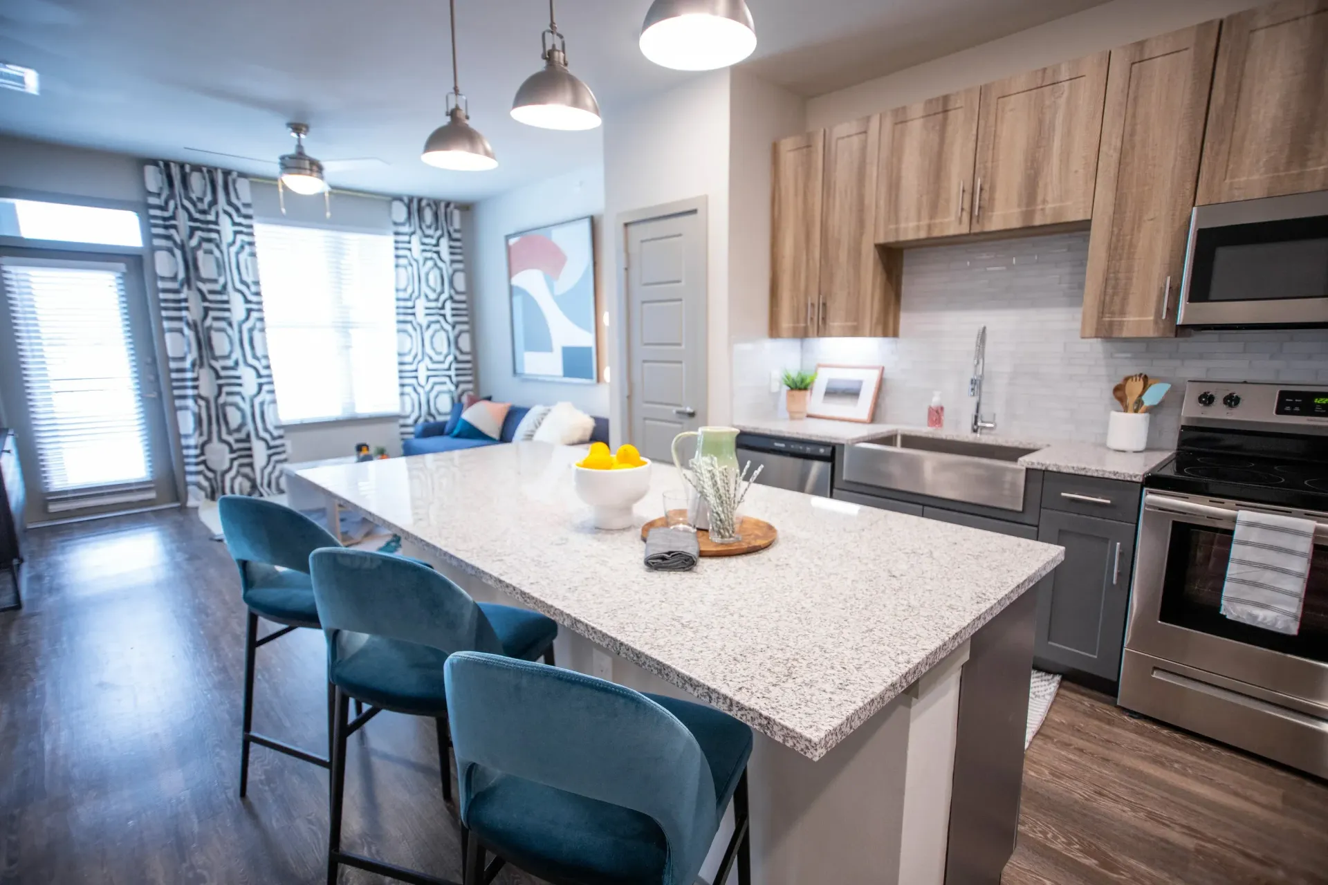Open-plan kitchen in a modern apartment with a large granite island and blue bar stools.