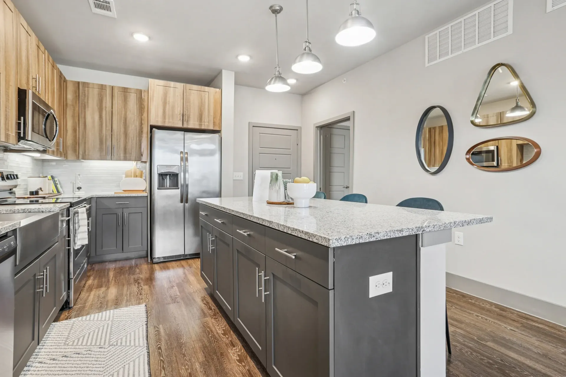 Modern kitchen with a large island, wood-toned upper cabinets, gray lower cabinets, and stainless appliances.
