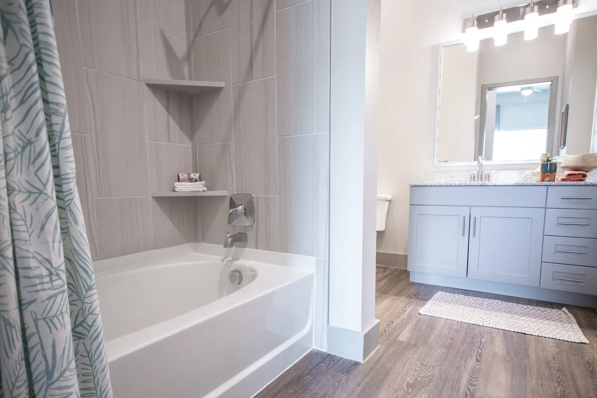 Bathroom with tub, tiled shower area, shower curtain, and gray vanity with a large mirror.