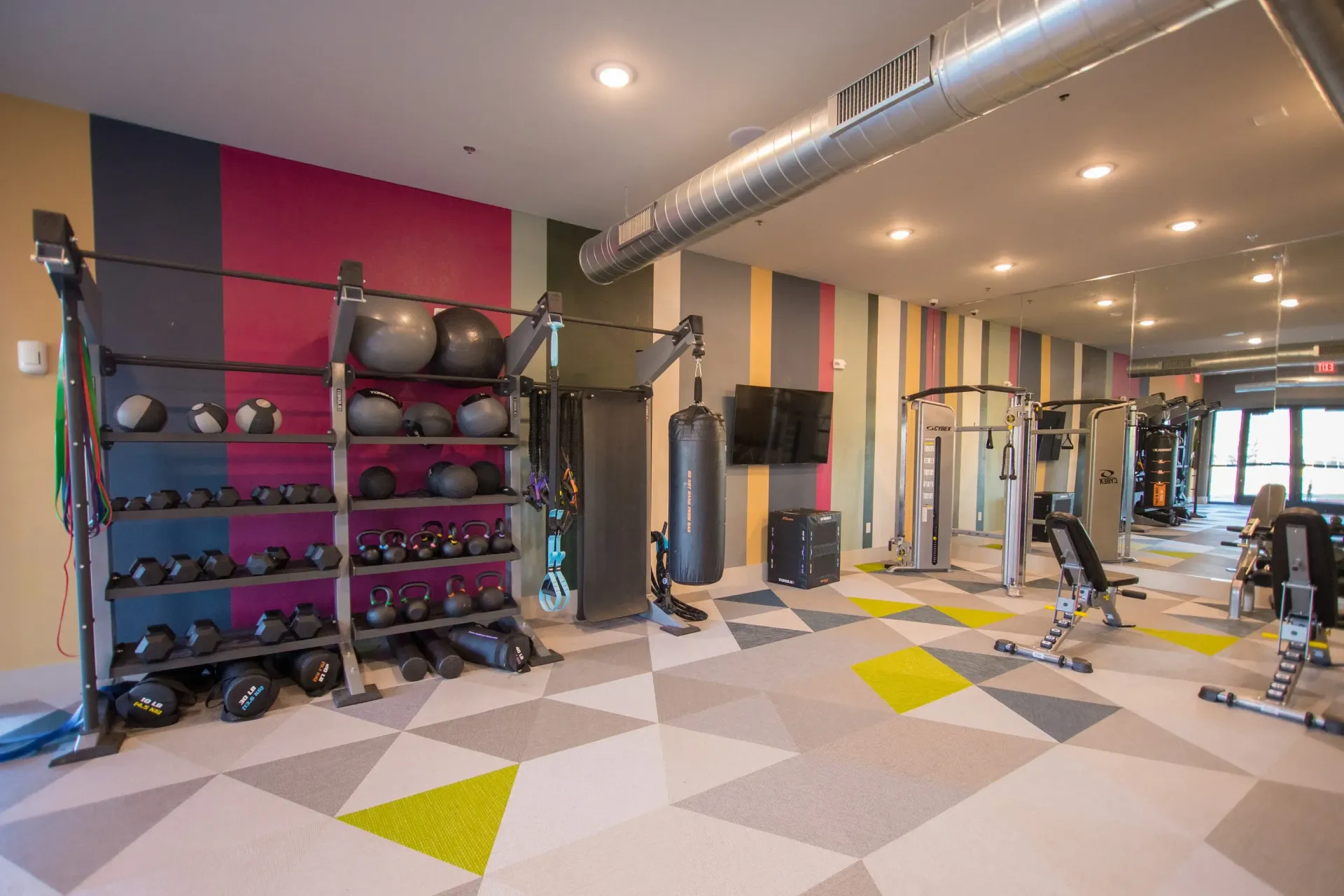 Interior view of a colorful apartment community gym with weights, kettlebells, and a punching bag.