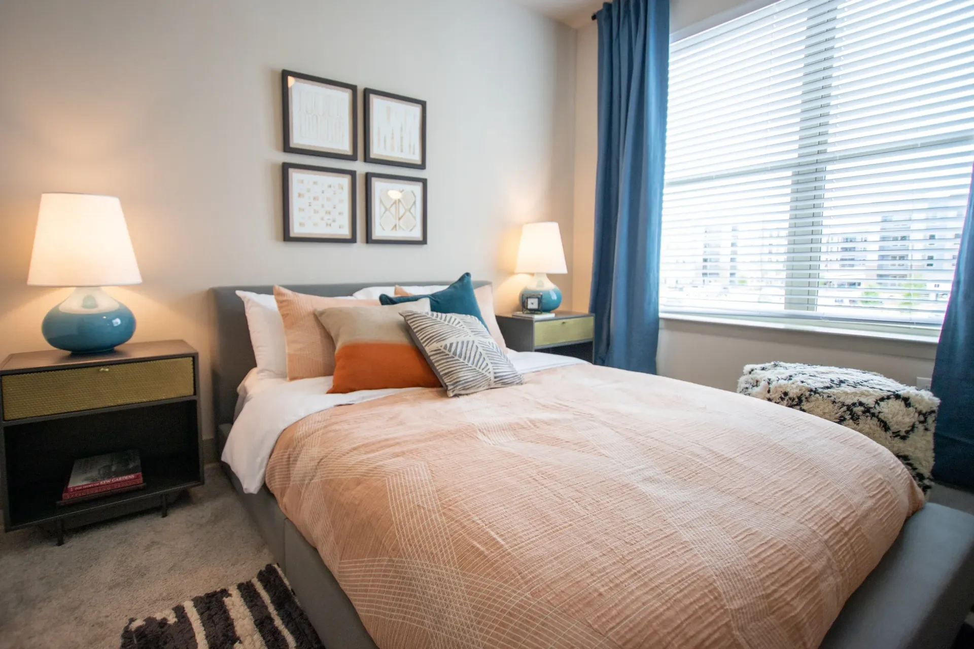 Bedroom with a plush bed, pastel bedding, two matching nightstands, and a large window with blinds.