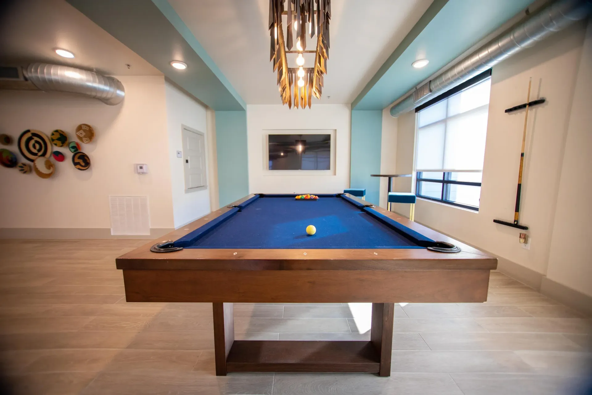 Indoor community game room with a blue pool table, chandelier, and large window.