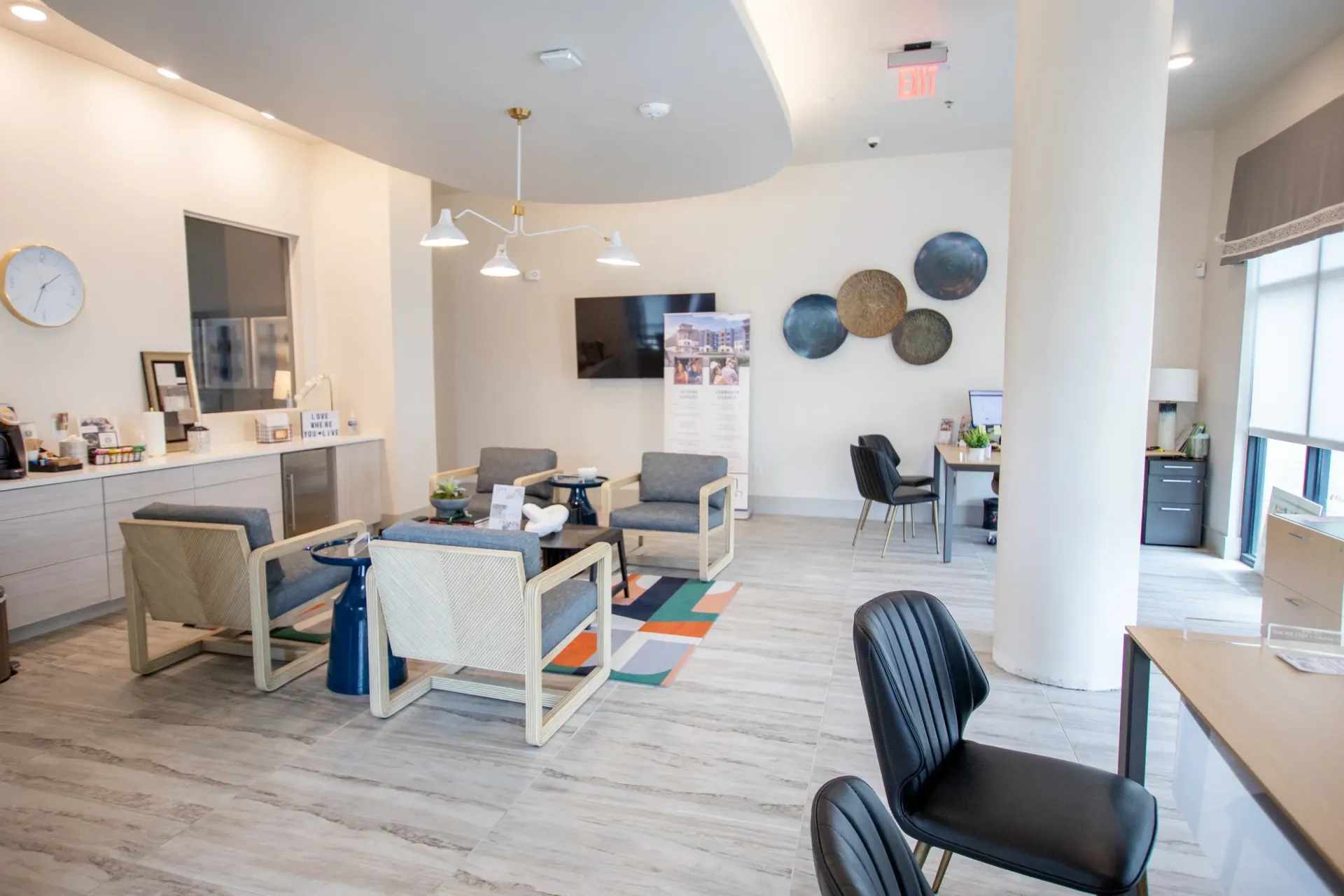 Bright community lobby with beige walls, gray seating, a reception desk, and large windows.
