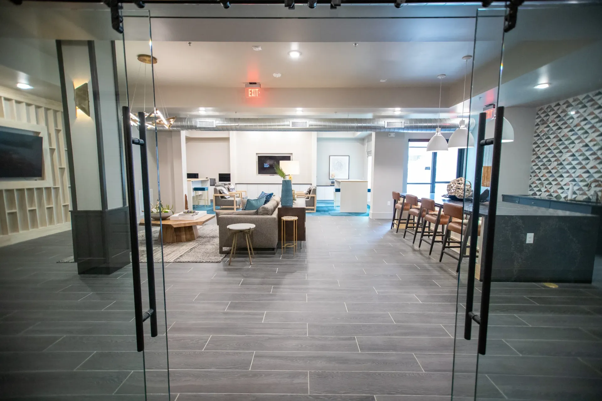 Interior of a modern apartment community lounge with sofas, tables, and a bar-height seating area.