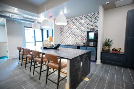 A modern kitchen lounge features a long dark marble island with four leather stools, pendant lighting, and a patterned wall.