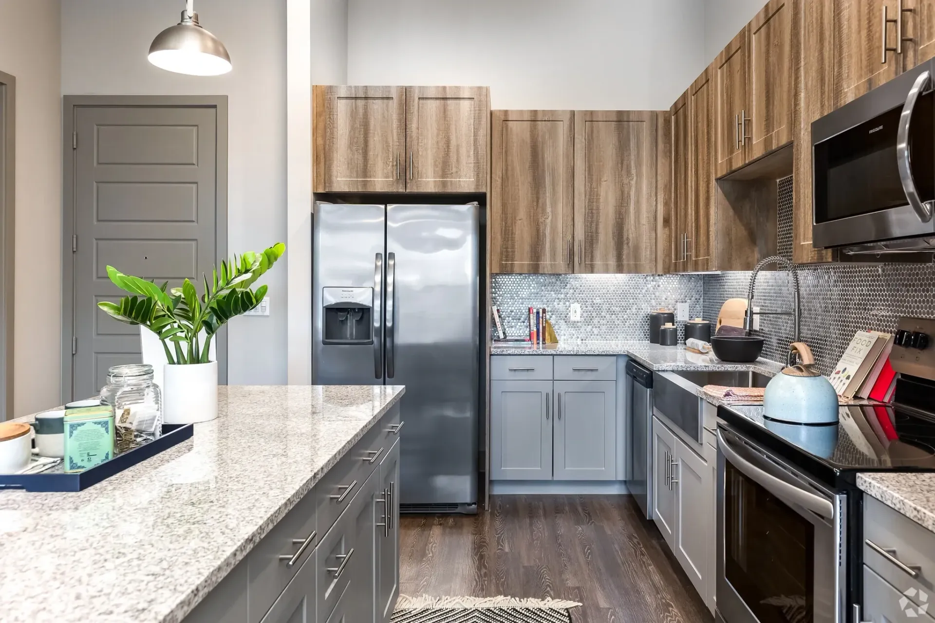 Modern apartment kitchen with gray cabinets, stainless-steel appliances, and speckled countertops.