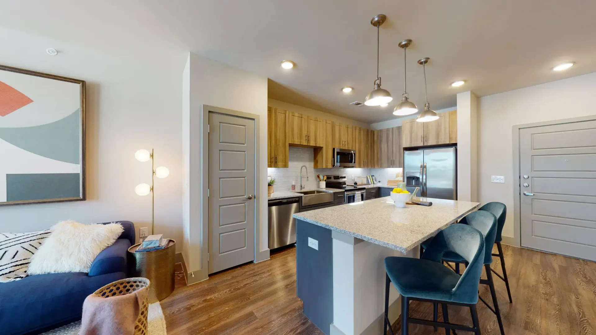 Open-concept kitchen with island, pendant lights, stainless steel appliances, and a blue sofa in the living area.
