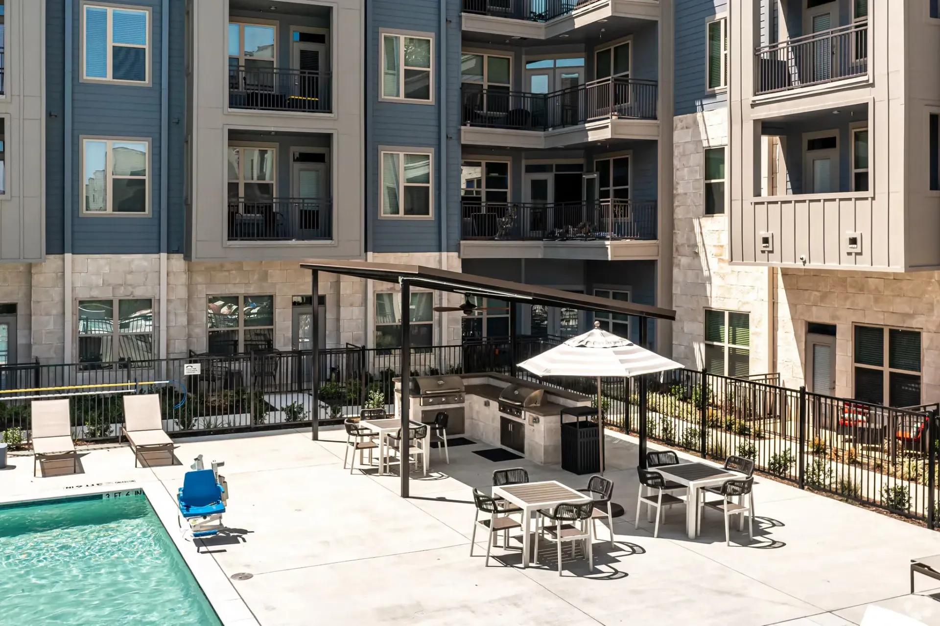 Outdoor pool courtyard with lounge chairs, grills, and umbrellas at a modern apartment complex.