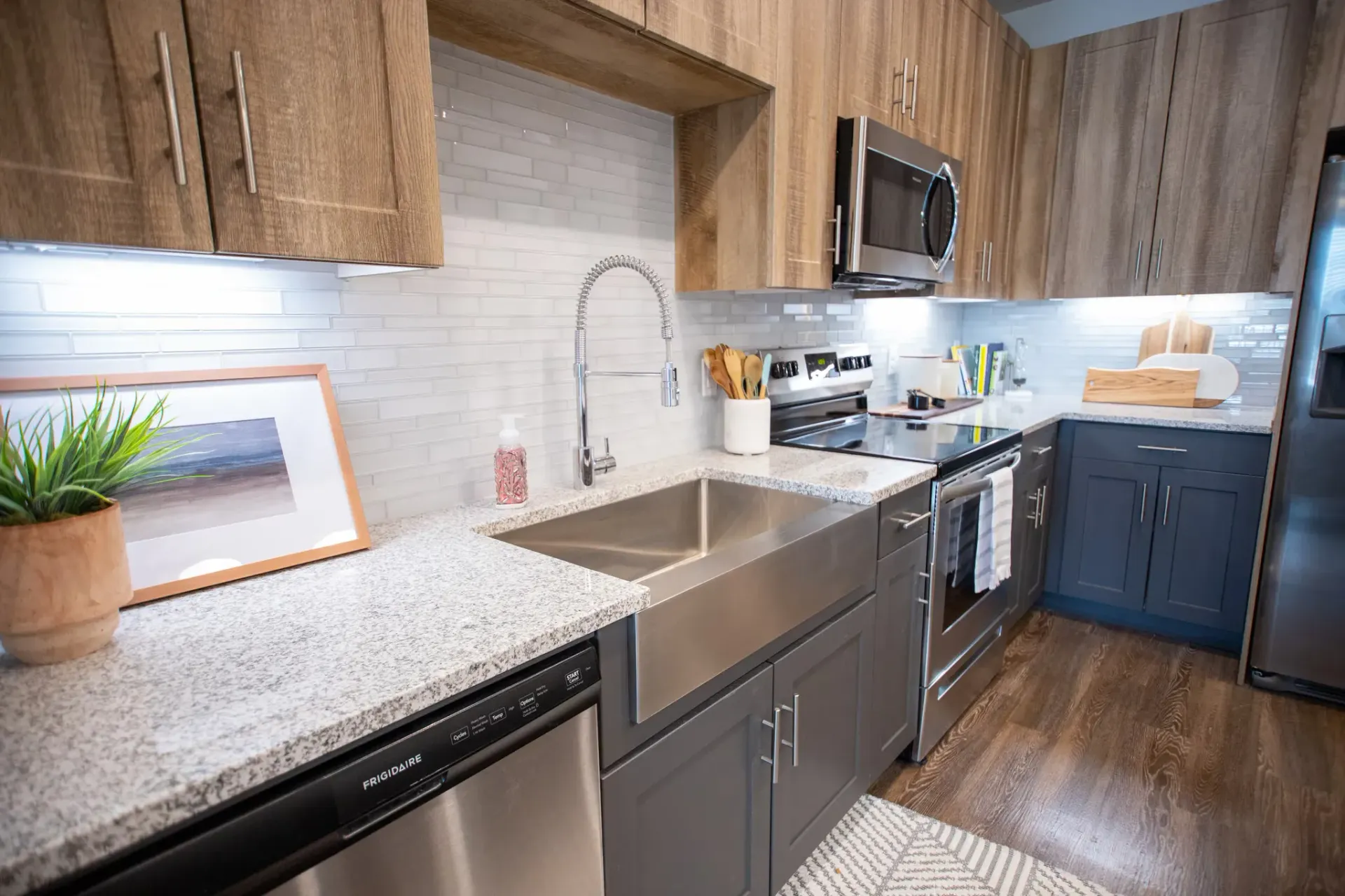 Modern kitchen with a large stainless-steel sink, gooseneck faucet, granite counters, and wood-toned cabinets.