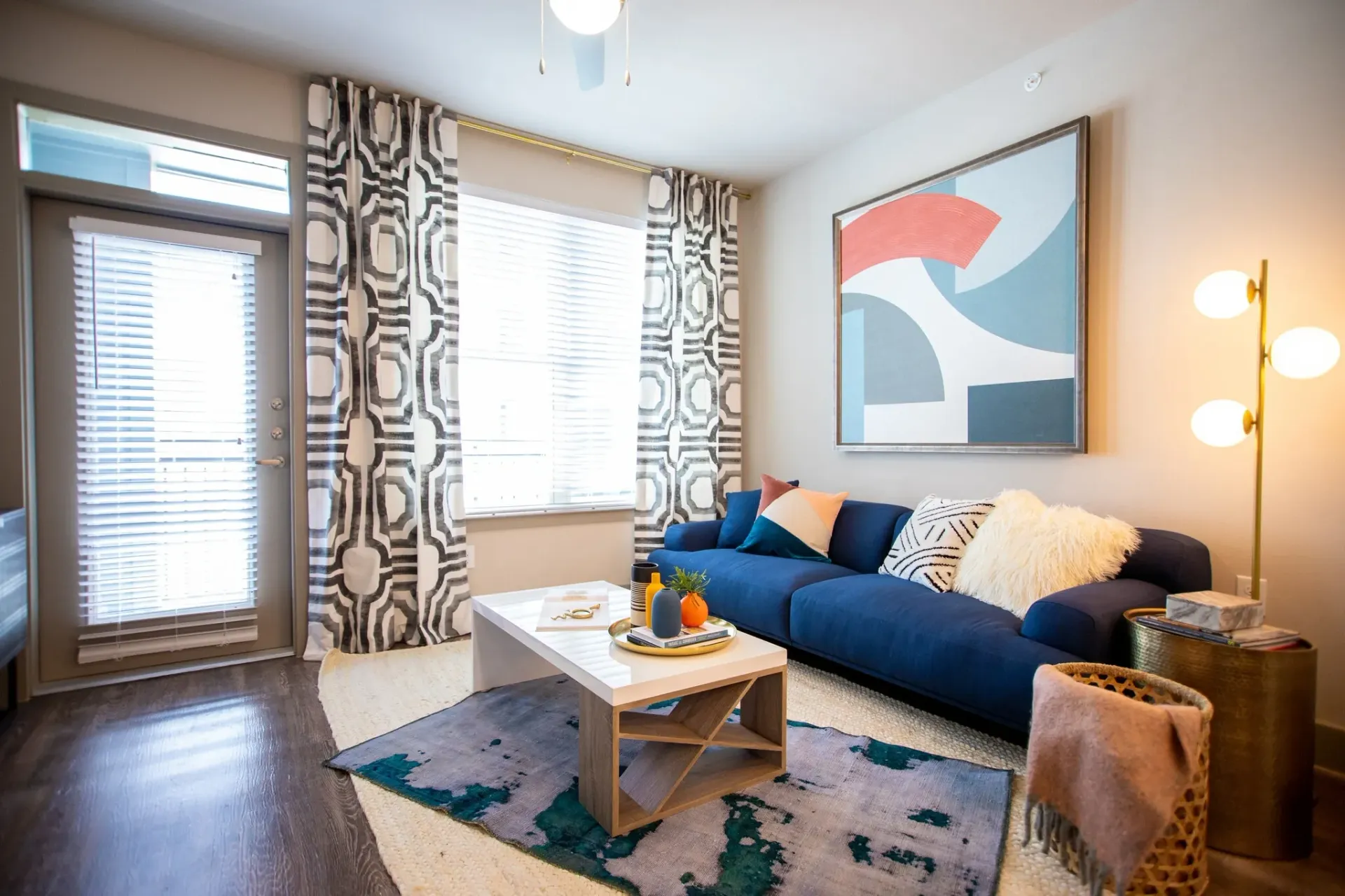 Interior living room with blue sofa, abstract art, patterned curtains, and coffee table.
