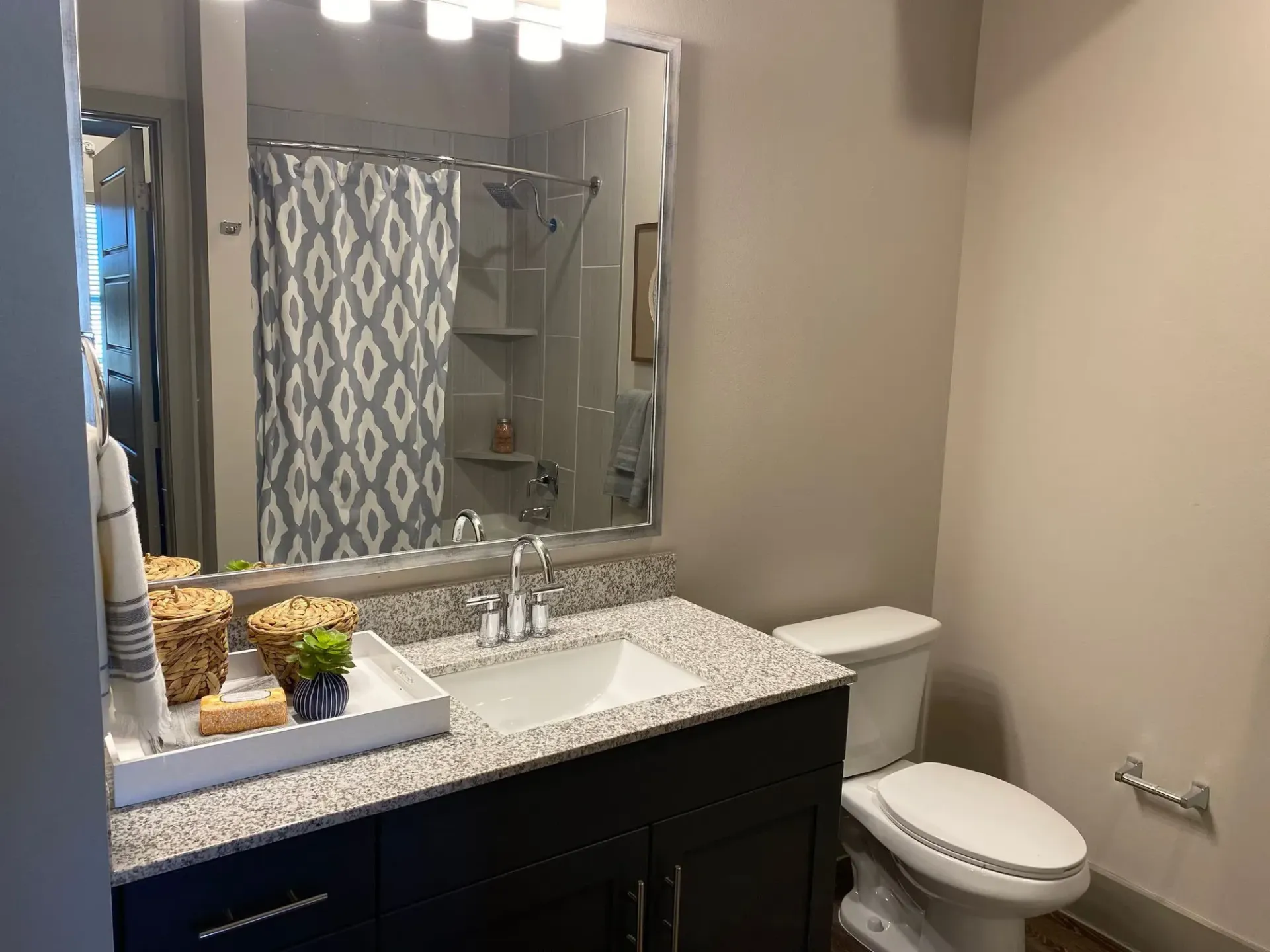 Bathroom with granite vanity, large mirror, toilet, and shower with a blue patterned curtain.