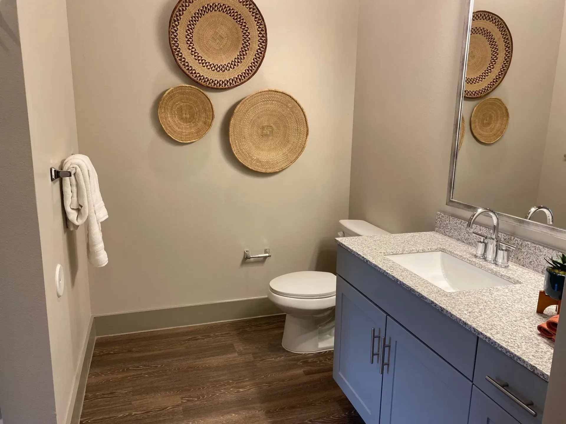 Bathroom with blue vanity, granite countertop, mirror, and decorative woven wall baskets.