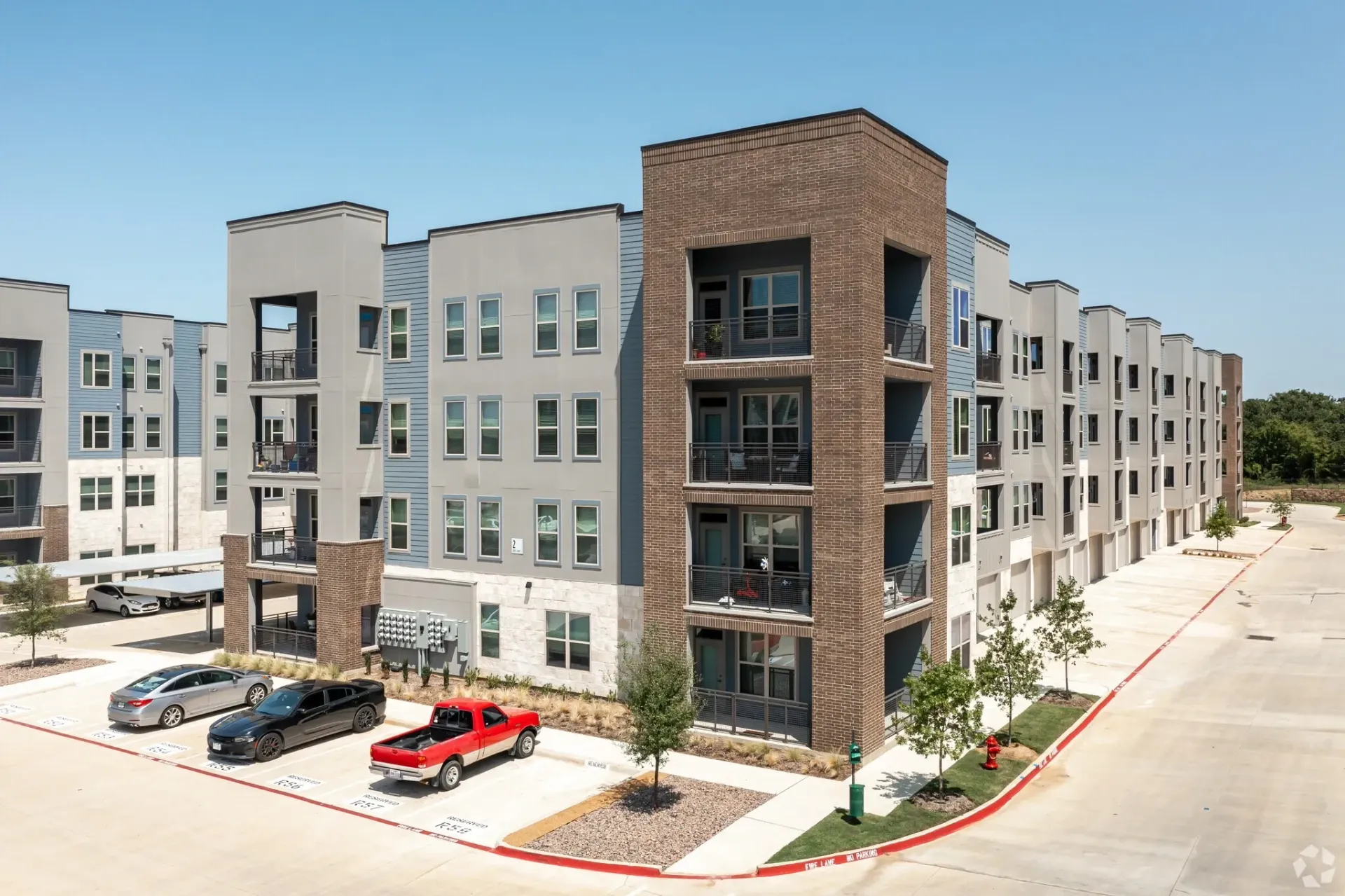 Exterior view of a modern apartment building with balconies and a parking lot.
