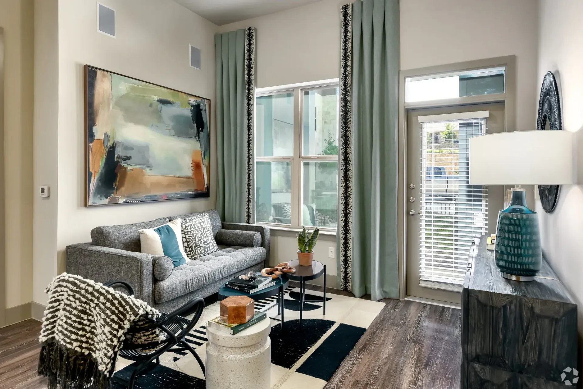 Living room in apartment with gray sofa, abstract wall art, and large window.