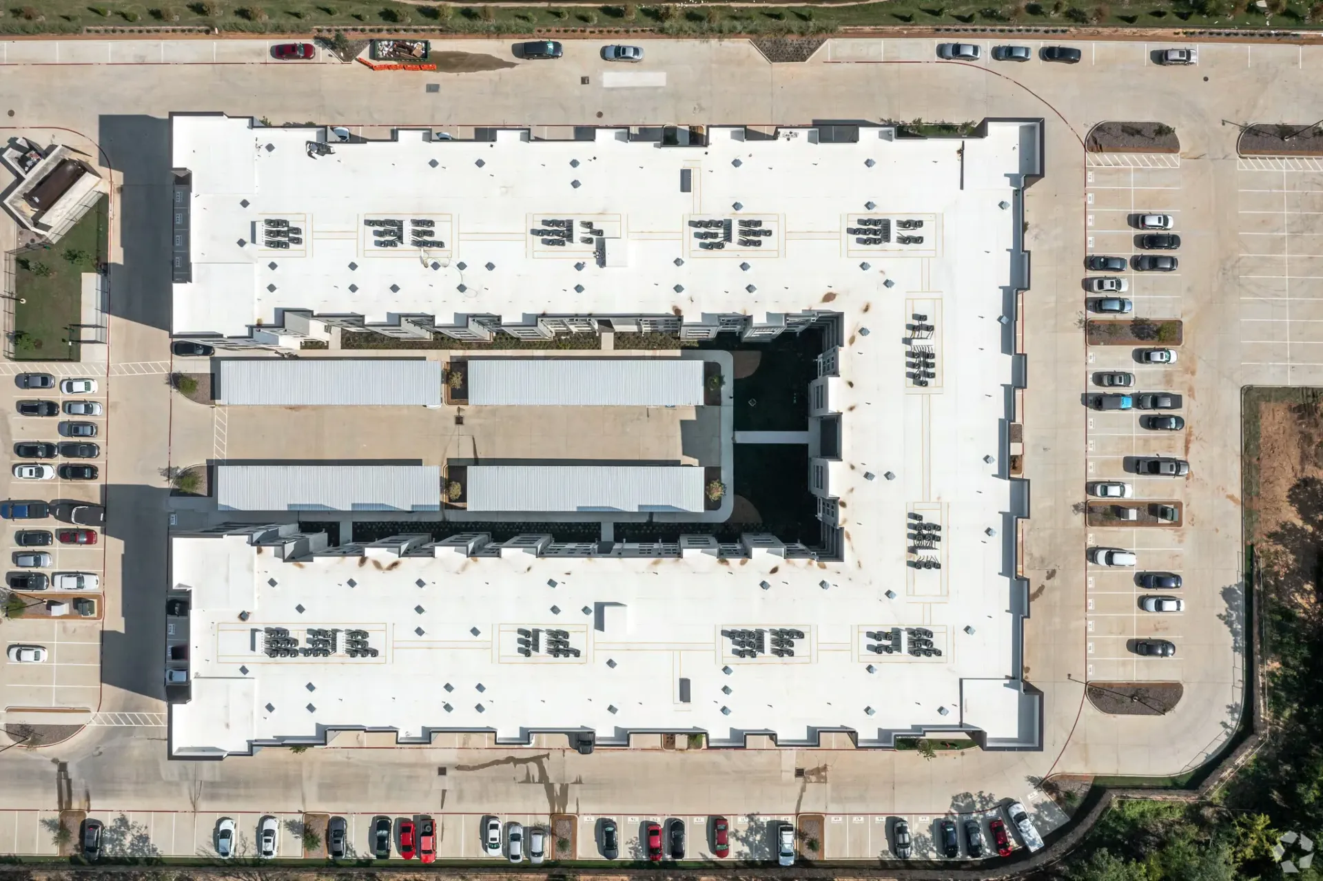 Aerial view of a large white U-shaped apartment building with surrounding parking.