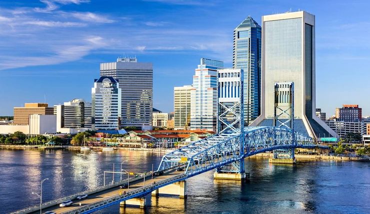 A man in a blue shirt and tie is smiling with his arms crossed