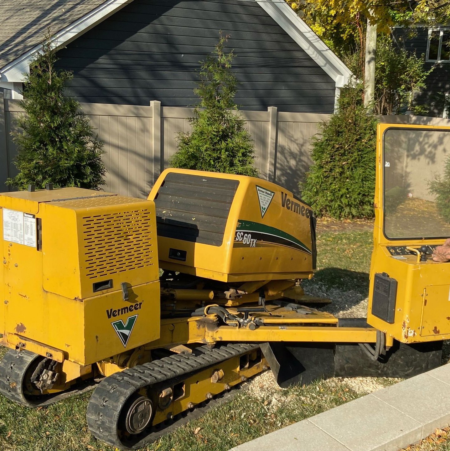 Yellow stump grinder on tracks, operated by a person wearing safety gear, in a yard.