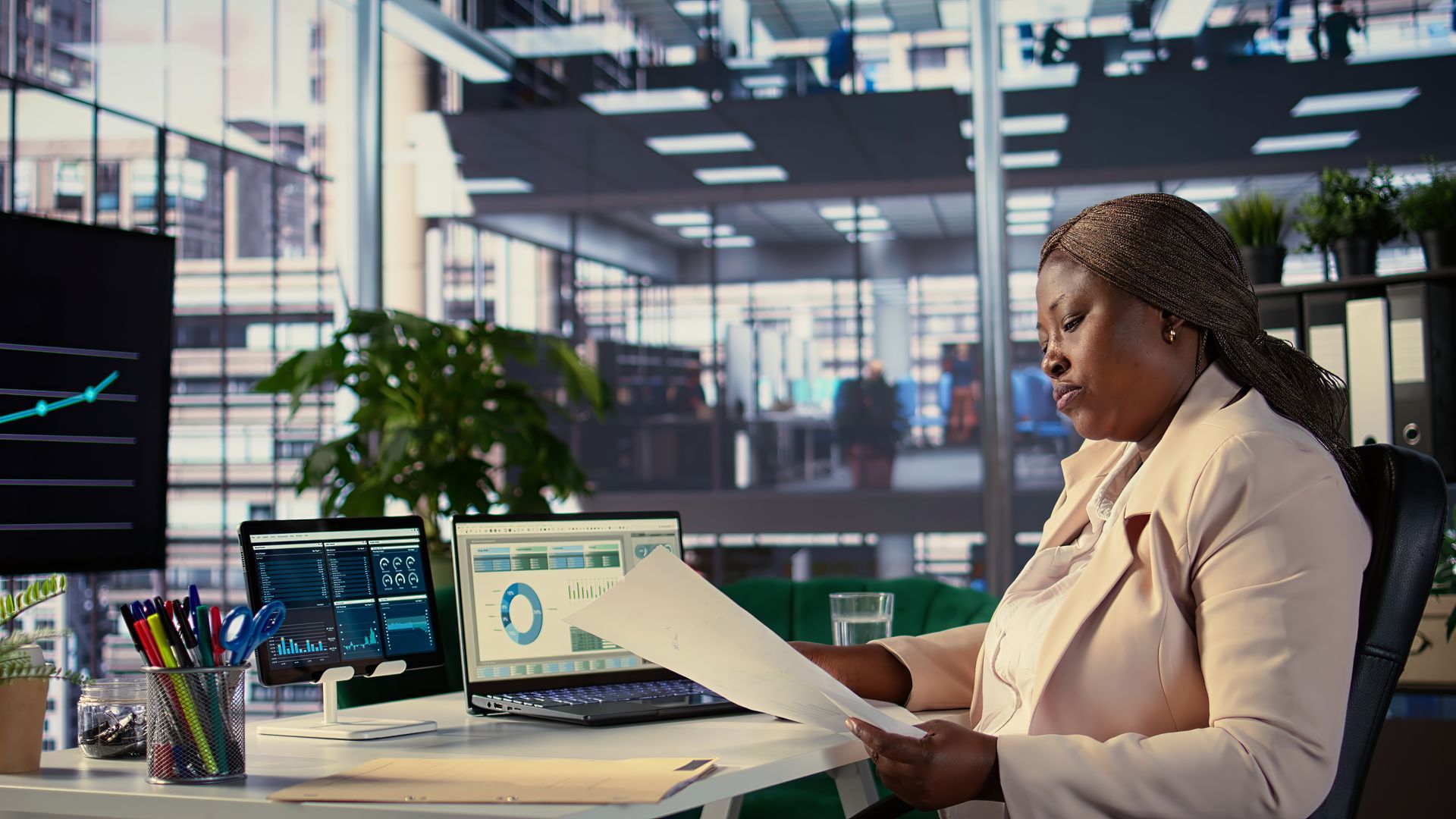 Office worker reviewing papers at a desk with multiple monitors in a modern workspace.