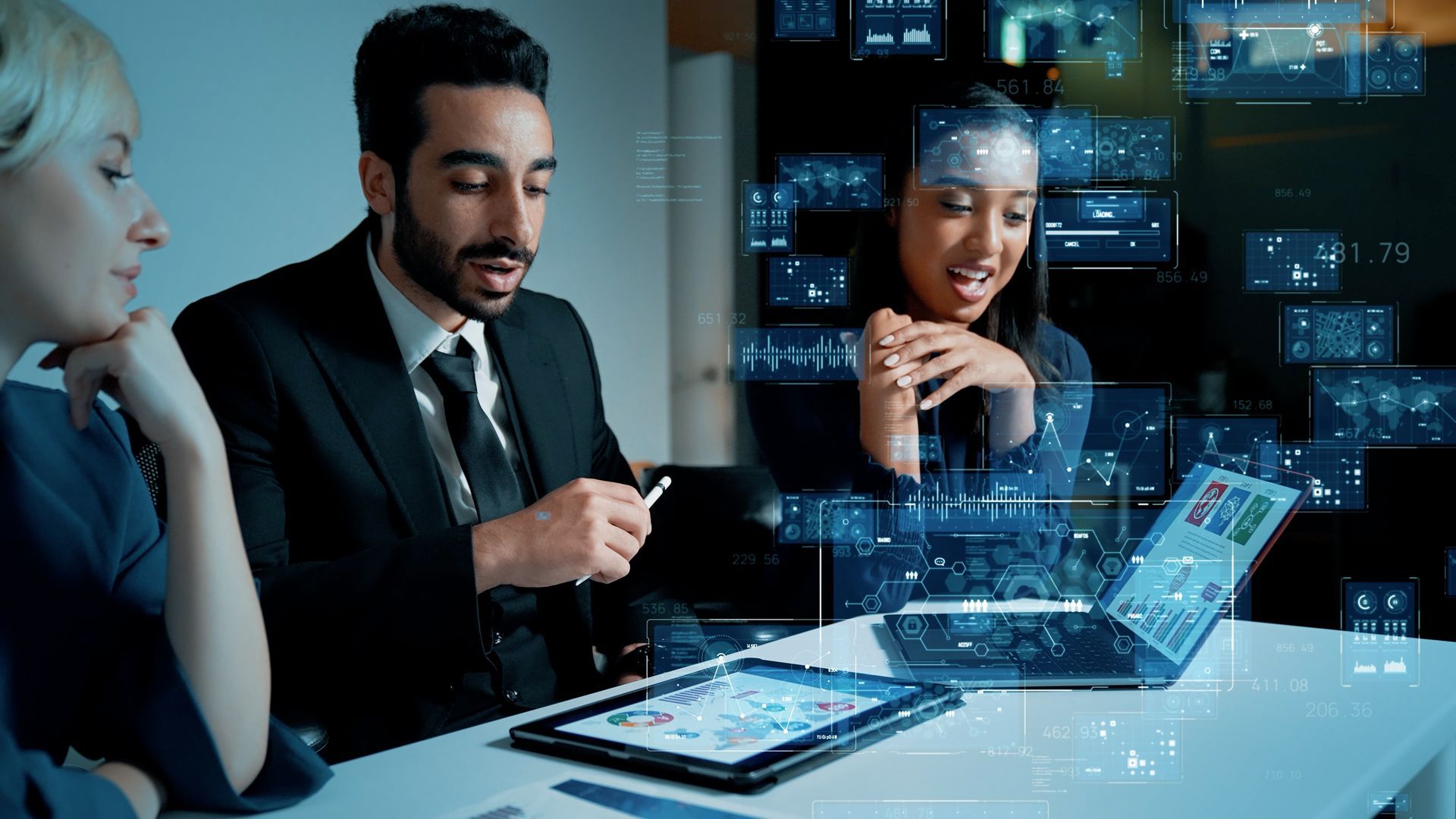 Three professionals in a modern meeting room discuss data on a glowing laptop and digital screens.