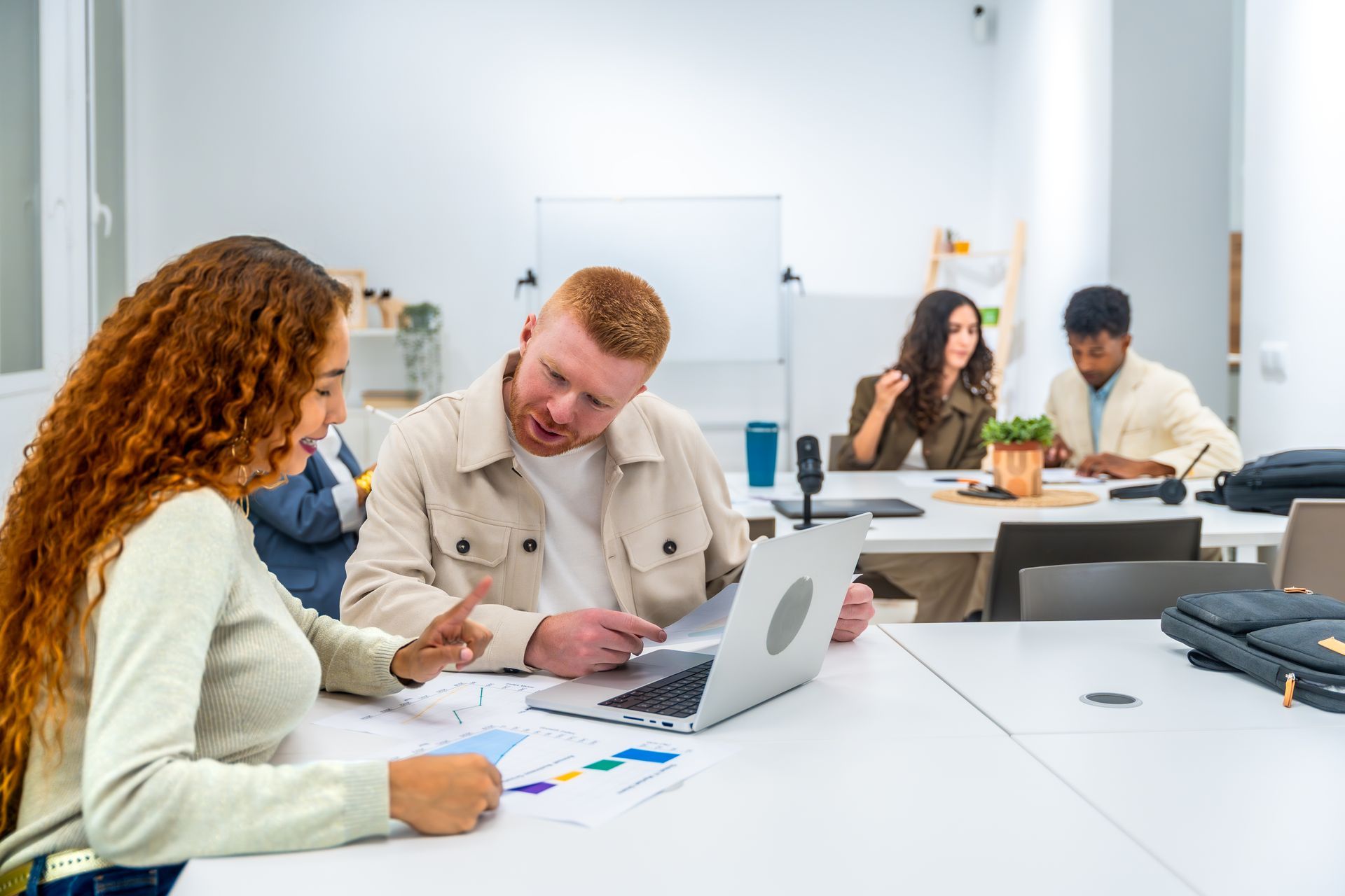 Coworkers collaborating at a bright office table with laptops, papers, and notes