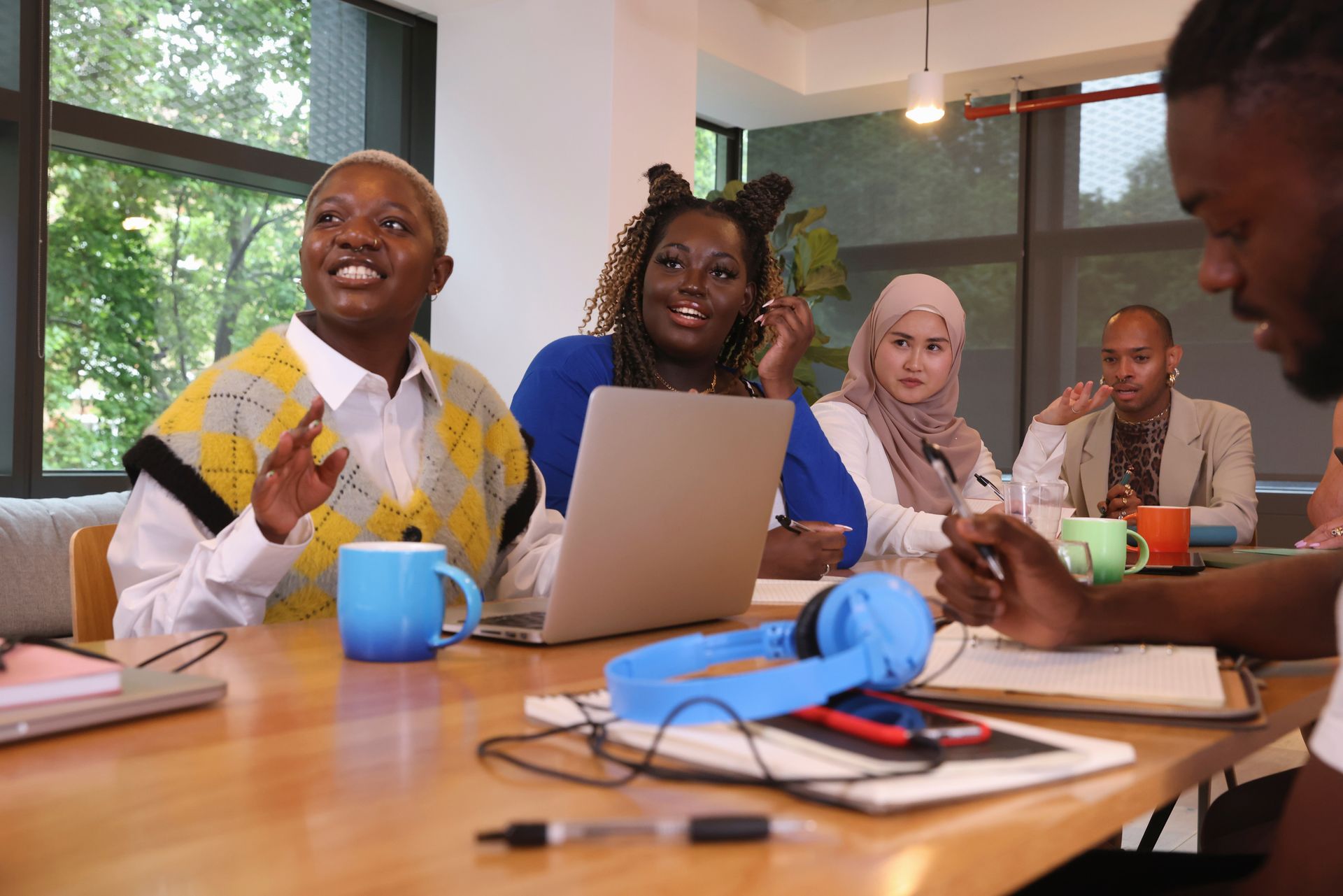 People collaborating around a laptop at a table in a bright meeting room, with notebooks and headphones.