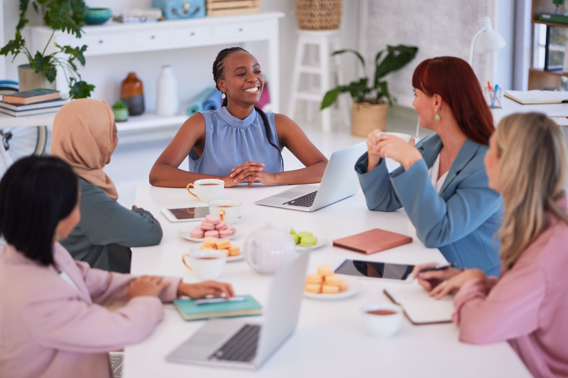 Small group in a bright office meeting around a table, discussing with notebooks and coffee cups.
