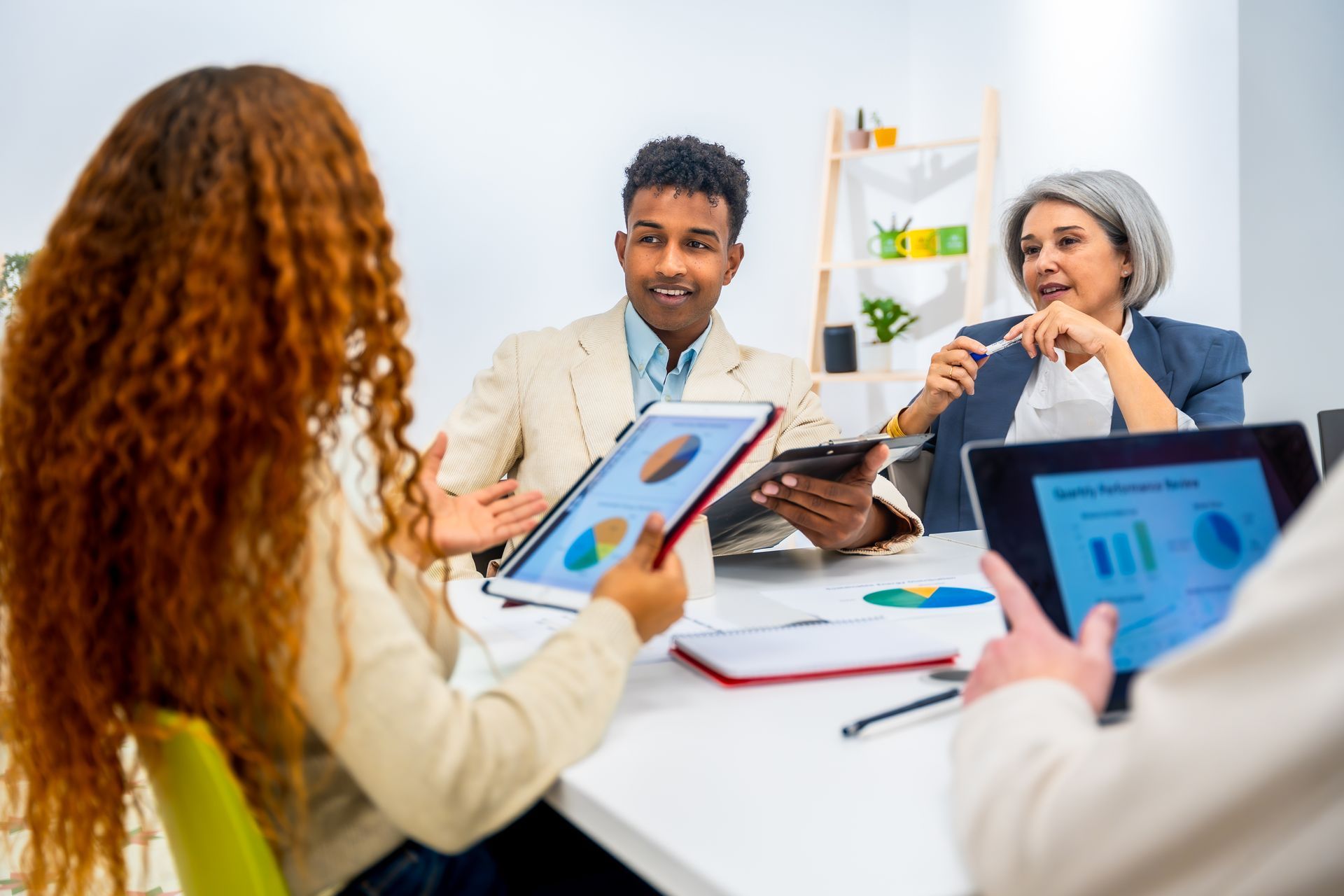 People in a meeting discussing tablet screens around a white conference table in a bright office
