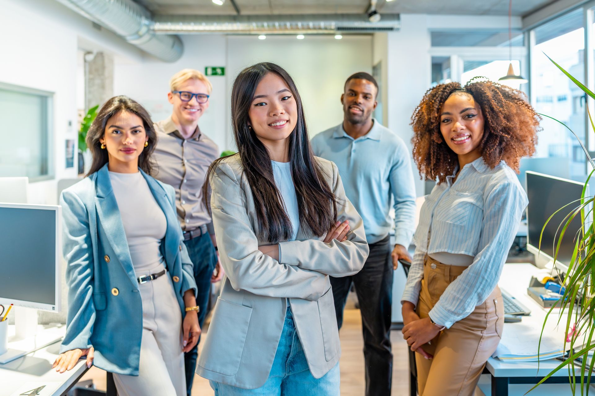 Five coworkers standing in a bright office, facing the camera with relaxed expressions.