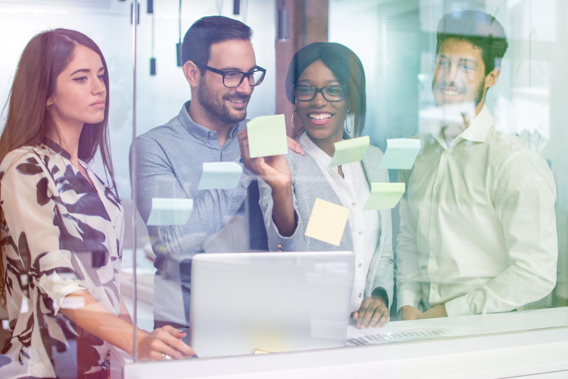 Team collaborating around a laptop with sticky notes on a glass wall in a bright office