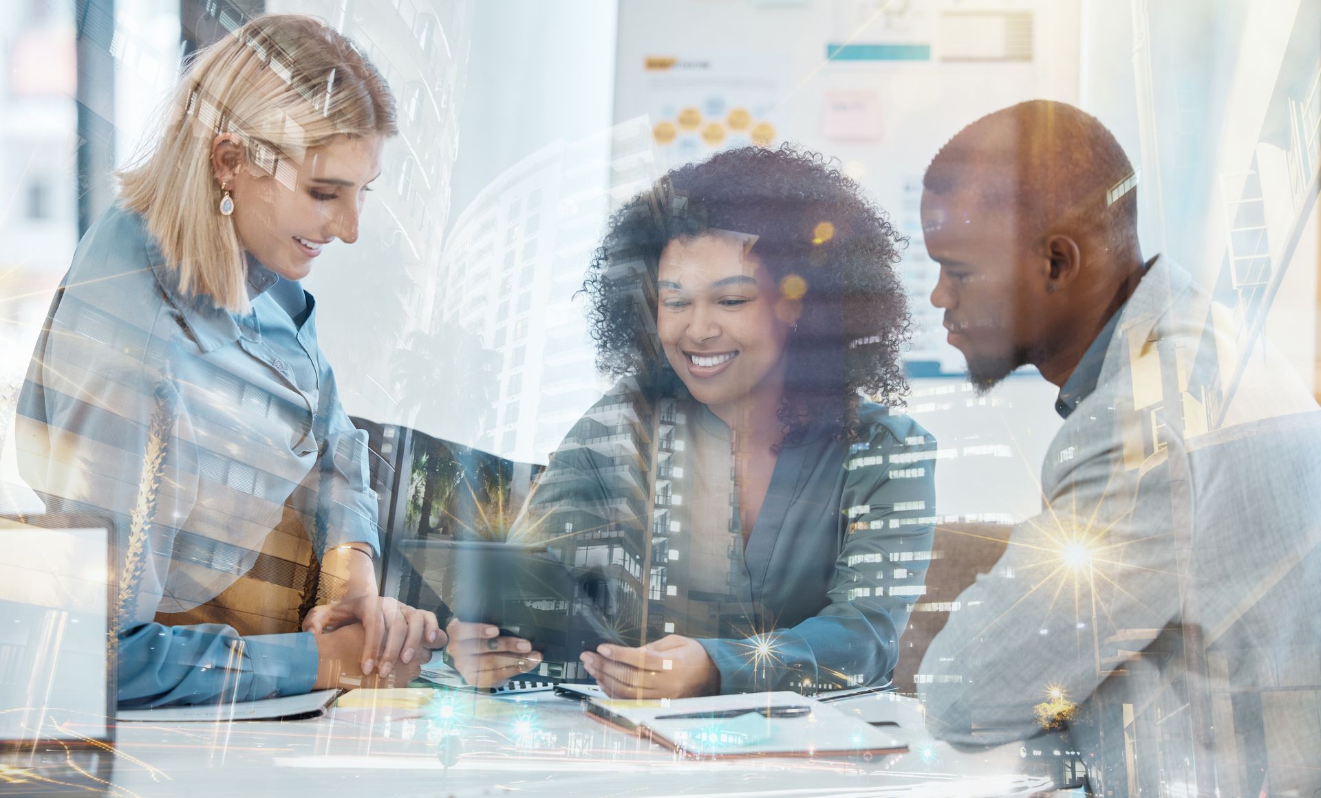 Three coworkers collaborate at a desk, reviewing documents on a laptop in a bright office.