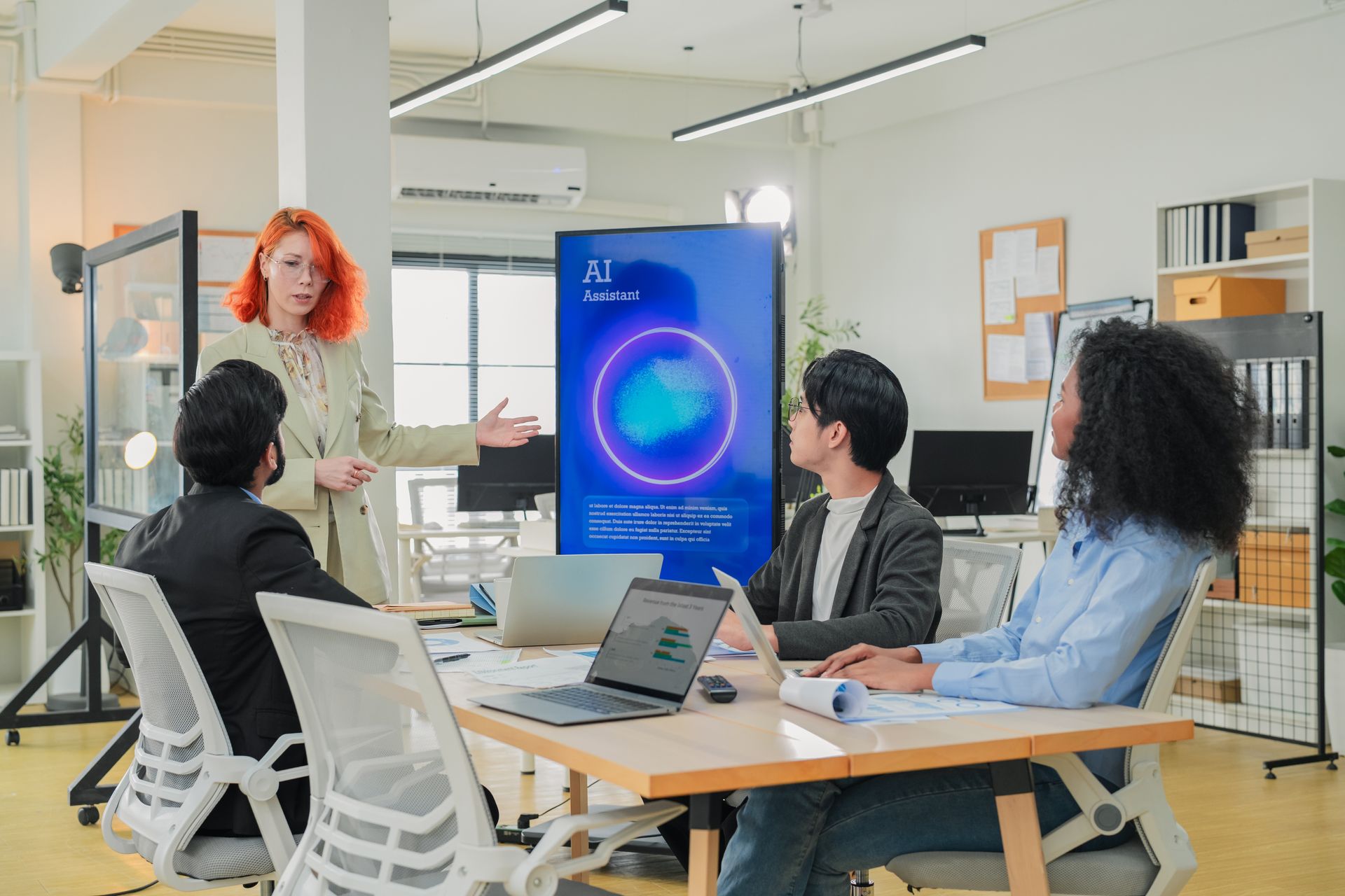 Team meeting in a bright office, with a presenter showing a blue chart on a large screen.