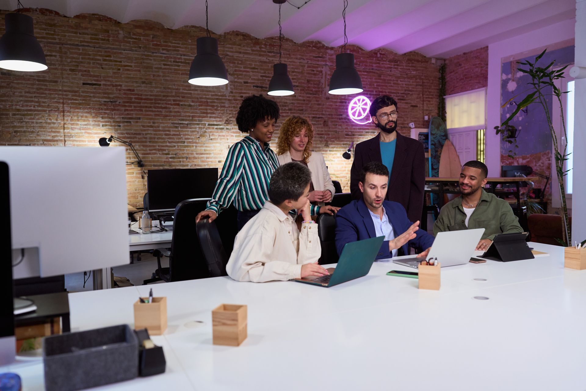 Team meeting around a laptop in a modern office with brick walls and hanging lights
