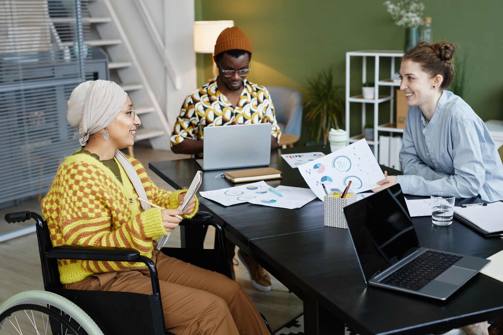 Three coworkers in a meeting around a laptop at a black table in a bright office