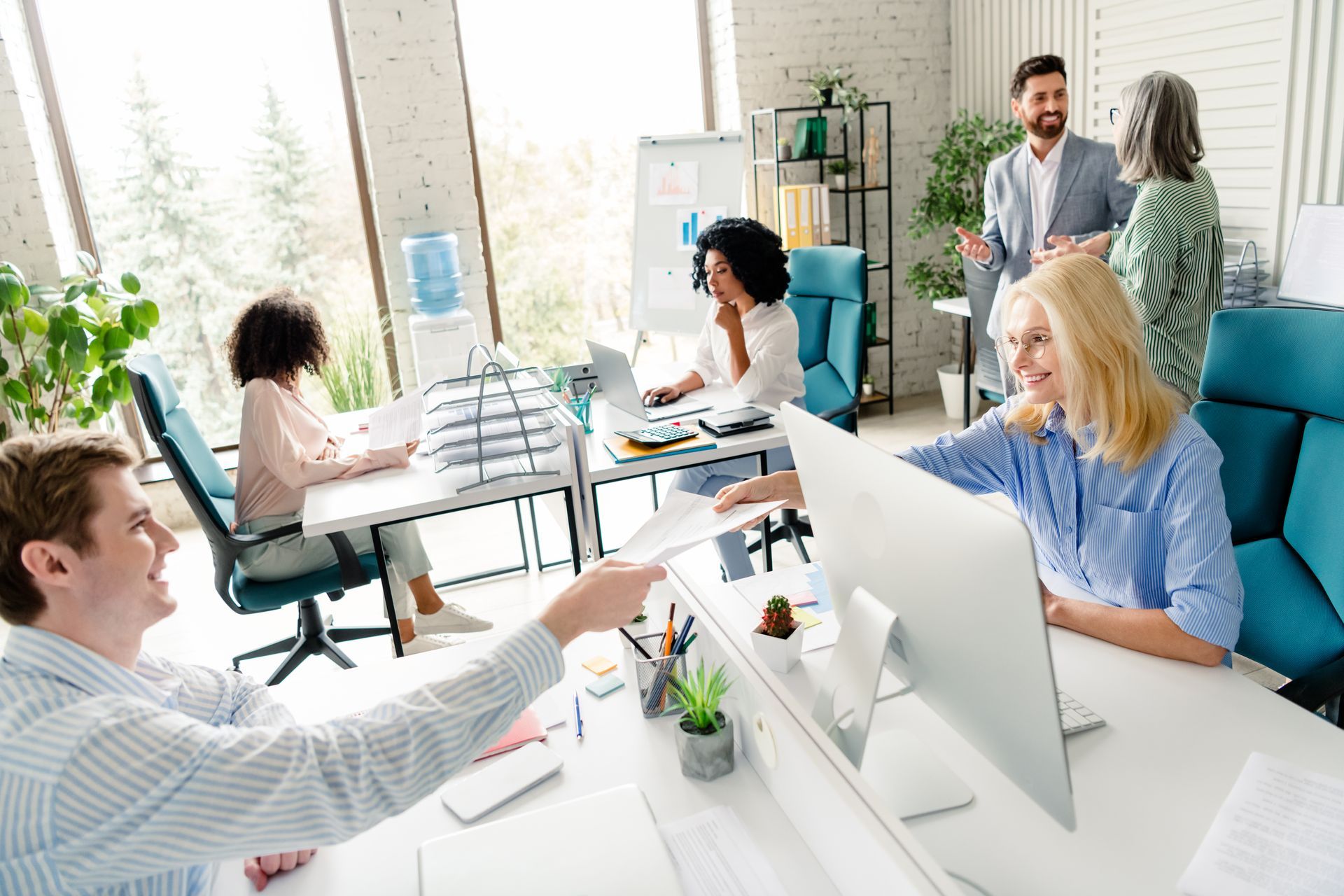 Team meeting in a bright office with people gathered around desks and computers