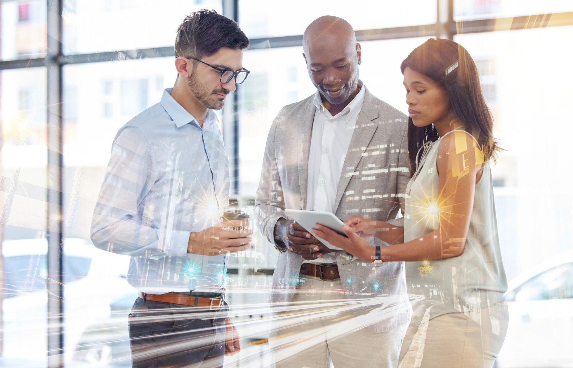 Three coworkers discussing a tablet in a bright office, with charts reflected on the glass wall.