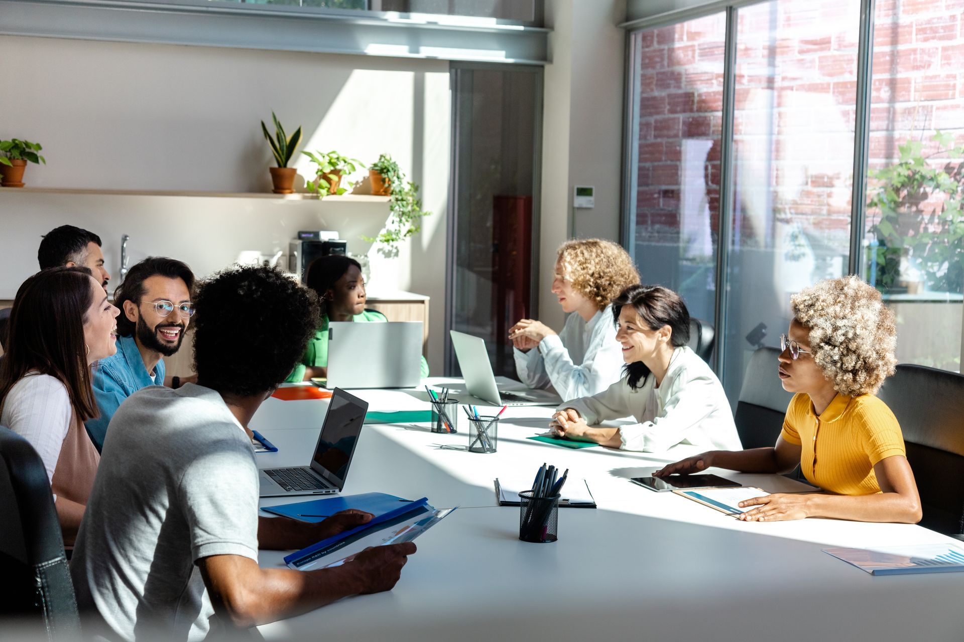People gathered around a bright office table in a meeting, discussing documents and laptops.