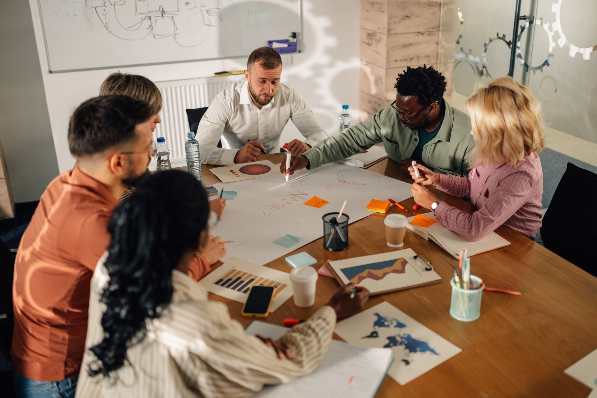 Team collaborating around a conference table with papers, tablets, and coffee in a bright office meeting room