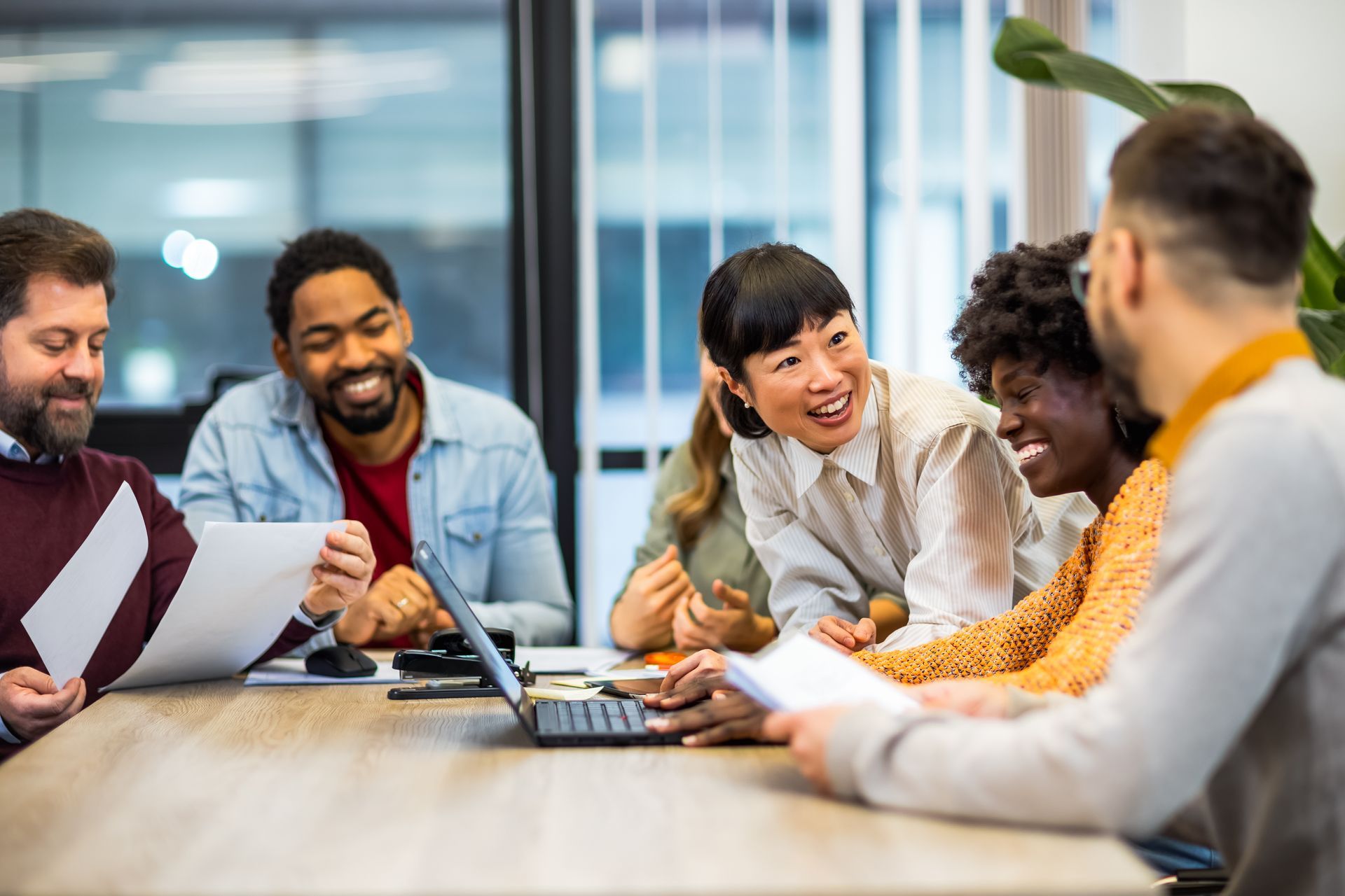 Colleagues smiling and talking around a conference table with laptops in a bright meeting room