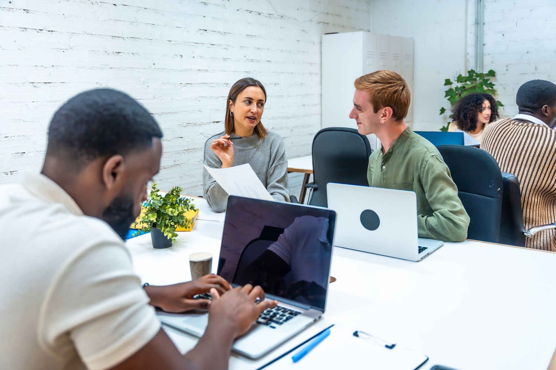 People collaborating at laptops and talking in a bright office meeting space