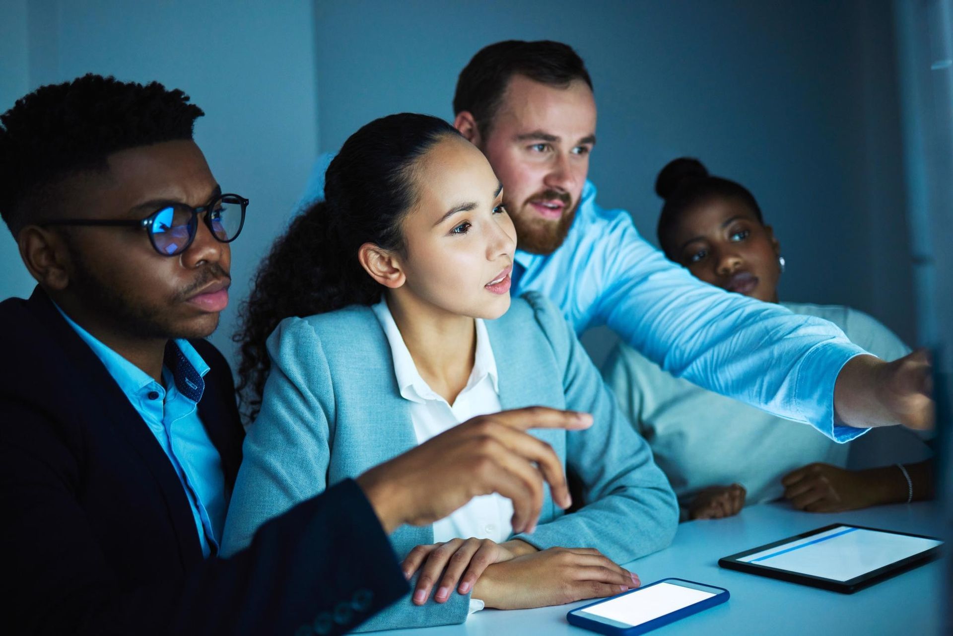 Colleagues in a meeting, pointing at a laptop screen in a dim office