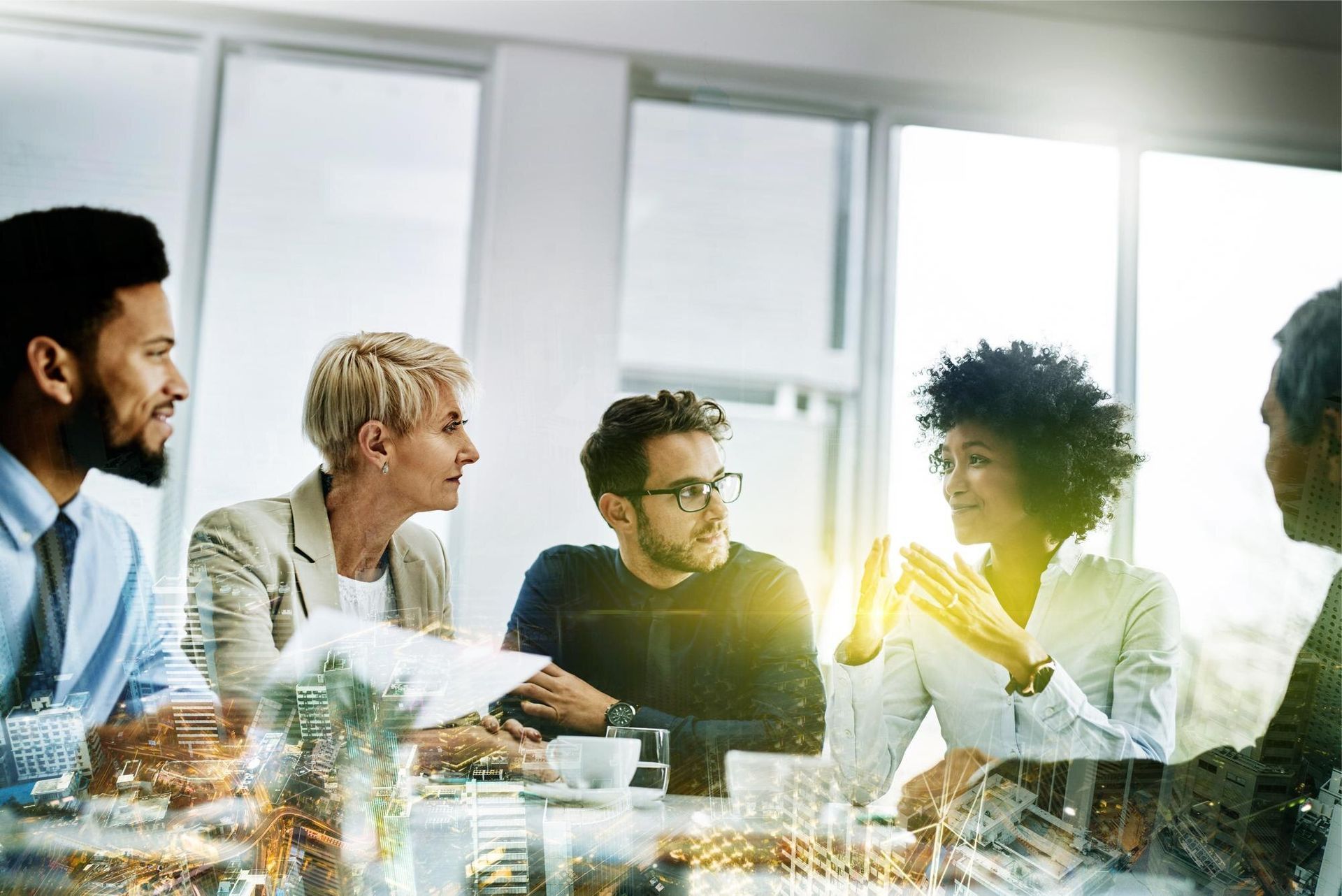 Group of coworkers discussing around a table in a bright office, with sunlight streaming in from the window.