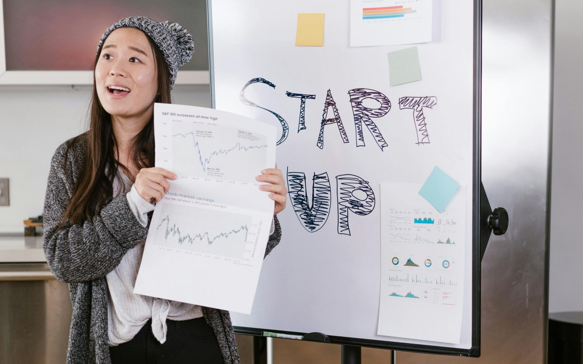 Woman presenting papers beside a whiteboard with “START UP” written on it