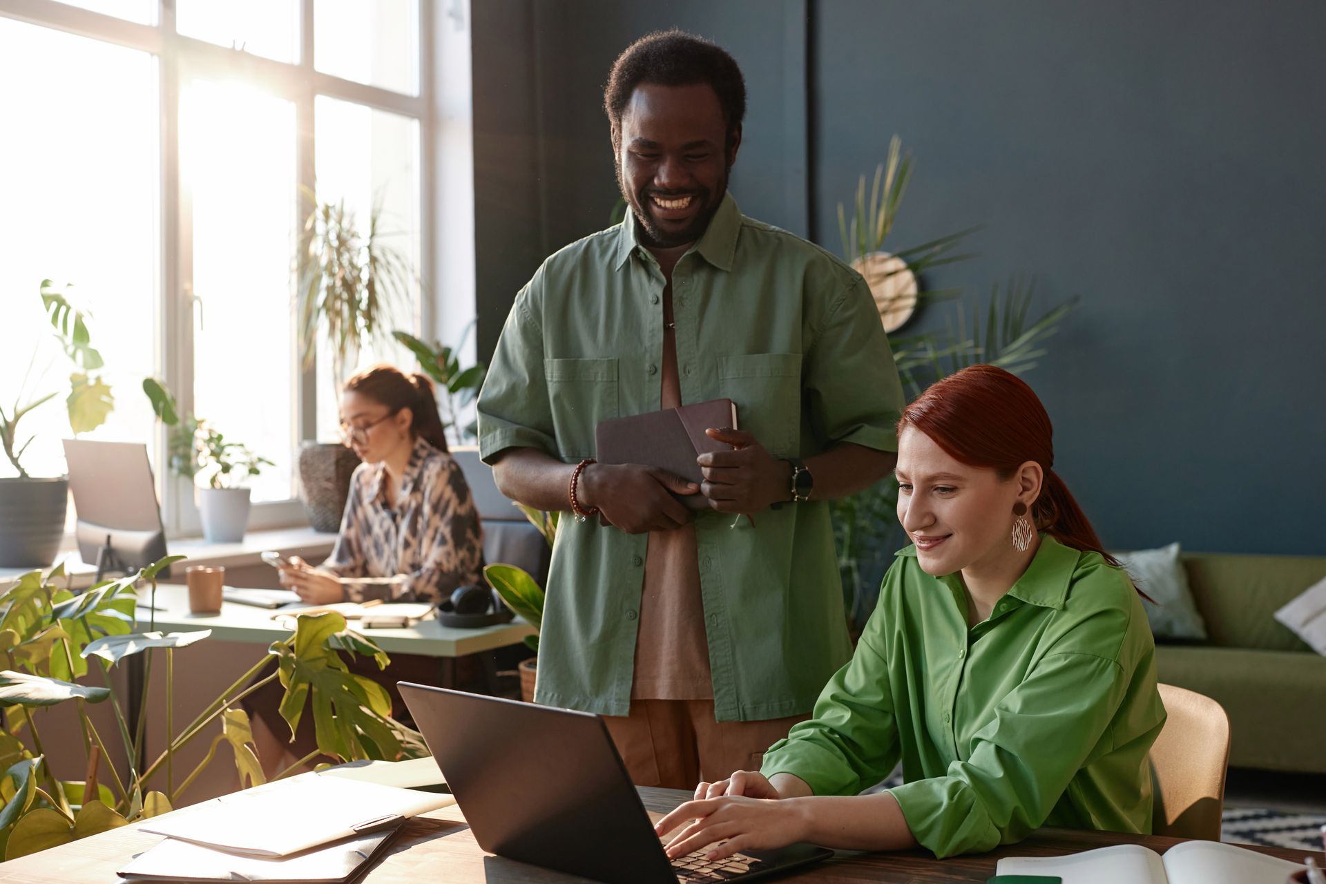 Coworkers collaborating in a bright office, with one using a laptop while others stand nearby.